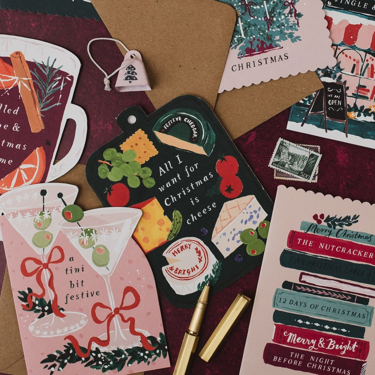 Bookish Christmas card with a stack of Christmas books on a deep red background, with martini and cheeseboard Christmas cards