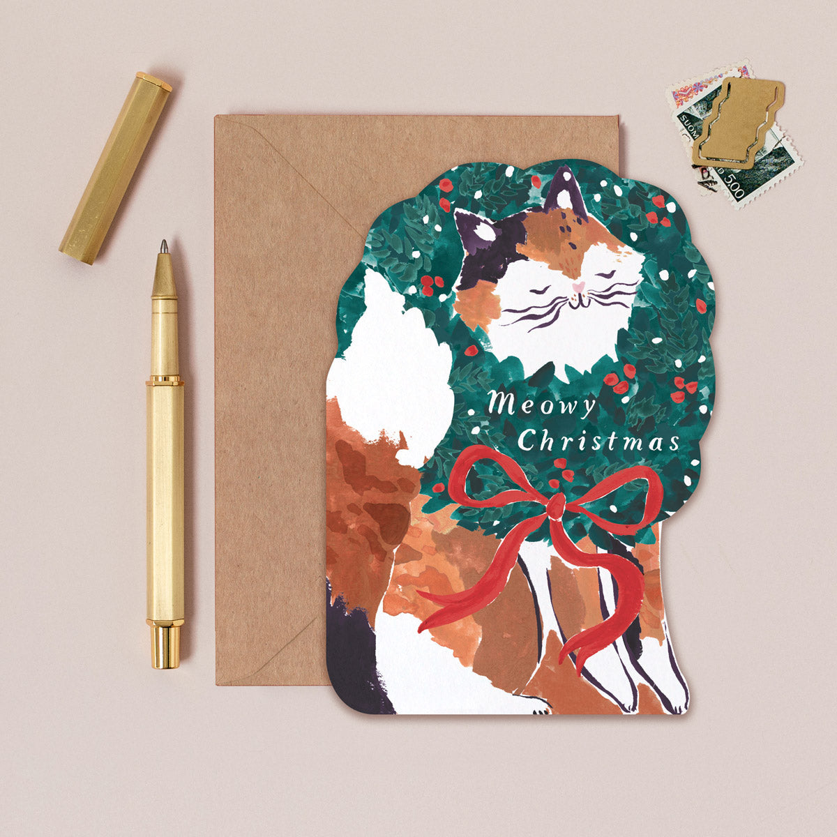 A Christmas card cut into the shape of a cat poking it's little face through a wreath from the Christmas card collection at Sister Paper Co.