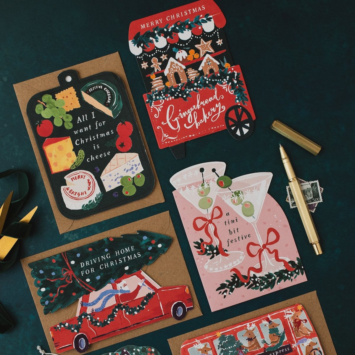 Cheeseboard shaped Christmas card on a dark teal background with gingerbread cart, martini and Driving Home for Christmas cards