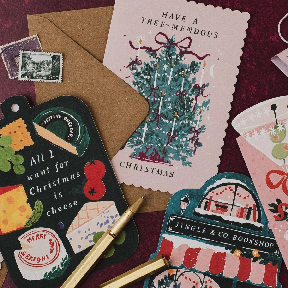 Jingle & Co bookshop shaped Christmas card on a deep red background with Tree-mendous and cheeseboard Christmas cards