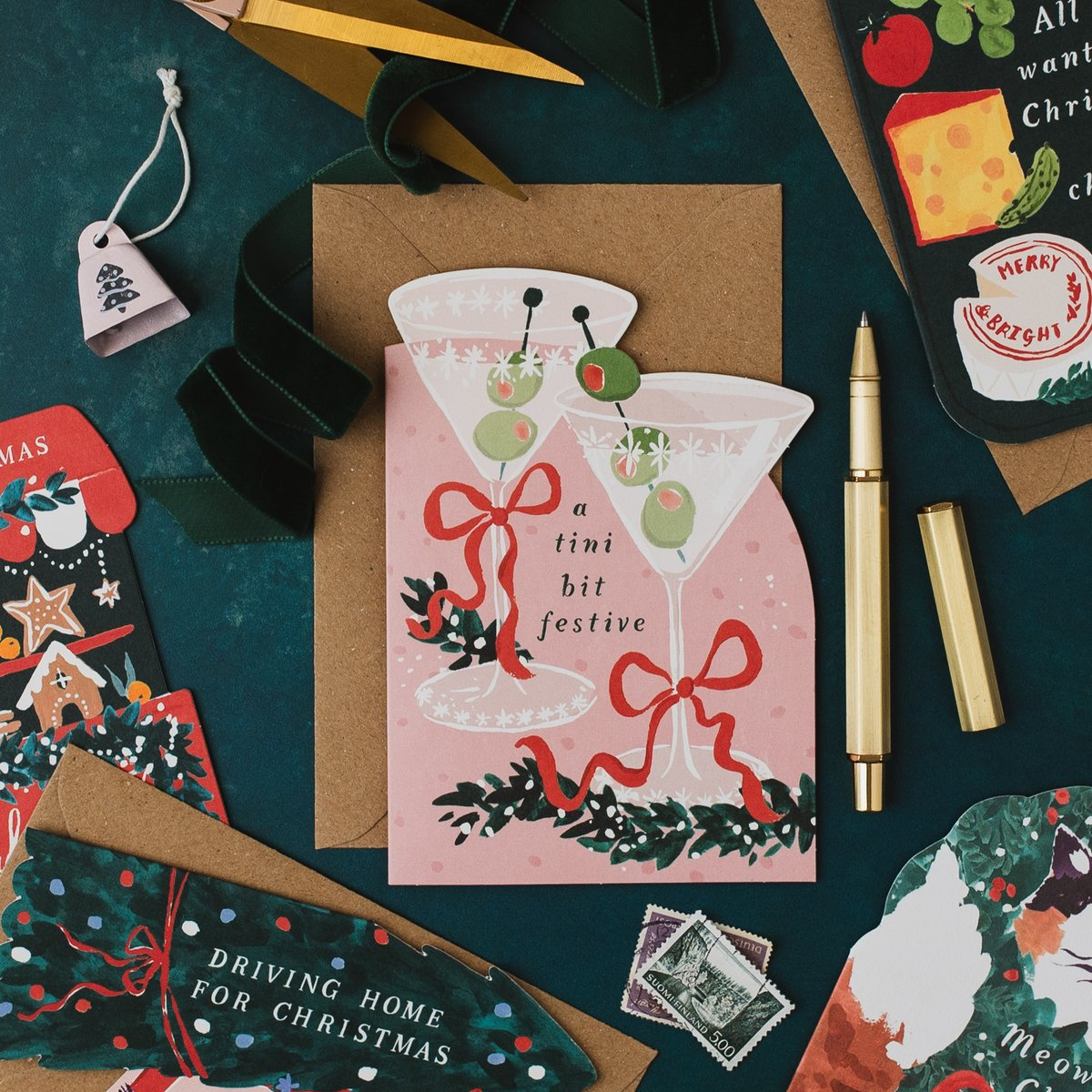 Tini Bit Festive martini Christmas card with a gold pen on a dark teal background, with Driving Home for Christmas and cheeseboard Christmas cards