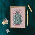 Christmas card with decorative tree and text on a dark green background with stationery items.