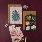 Have a Tree-mendous Christmas card with kraft envelope on a deep red background, with cheeseboard and martini Christmas cards