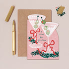 Christmas card with festive cocktail design, envelope, pen, and stickers on a beige background