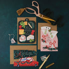 Cheeseboard, martini and Driving Home for Christmas shaped cards with kraft envelopes and gold scissors on a dark teal background