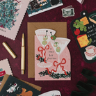 Tini Bit Festive martini shaped Christmas card with a gold pen on a deep red background, with Tree-mendous and cheeseboard Christmas cards