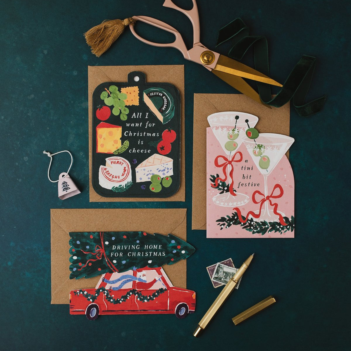 Driving Home for Christmas car shaped card with kraft envelope on a dark teal background, with cheeseboard and martini Christmas cards