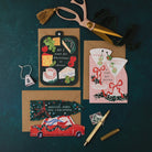 Driving Home for Christmas car shaped card with kraft envelope on a dark teal background, with cheeseboard and martini Christmas cards